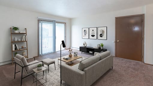 A living room with a grey couch, a chair, a small table with a vase and a plant on it, a bookshelf with a plant on top, and pictures on the wall.