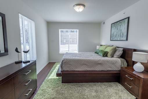 A bedroom with a bed, nightstand, and a window with blinds.