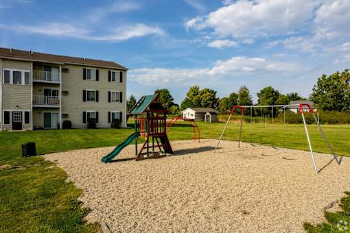 A playground with a green slide and a red swing set in front of a building.