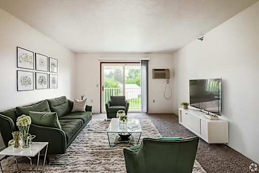 A living room with a green couch, a glass coffee table, and a flat screen TV.