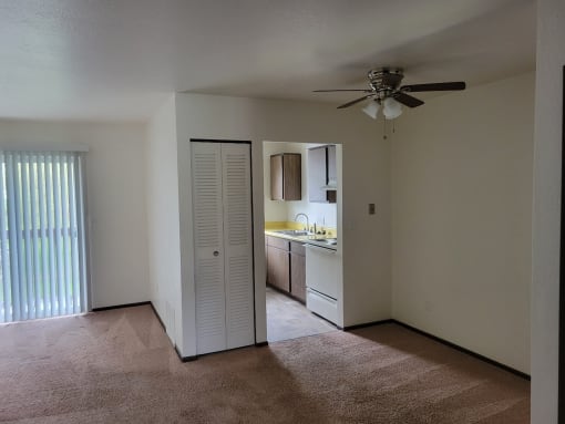 an empty living room with a ceiling fan and a kitchen
