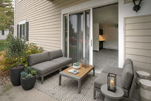 A grey couch sits on a patio with a table and a candle.