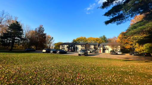 a house in the middle of a grassy field with cars parked in front of it