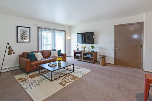 A living room with a brown couch, a coffee table, and a flat screen TV mounted on the wall.