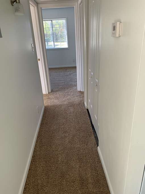 a hallway with a carpeted floor and white walls and a window