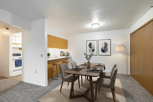 A dining room with a table set for two and a kitchen area in the background.