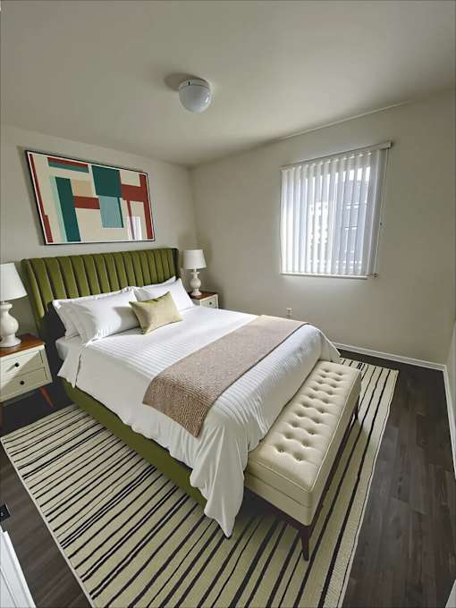 A bedroom with a bed, nightstand, and a painting on the wall.