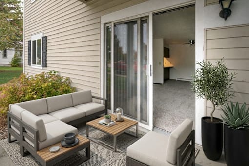 A patio with a grey couch, a wooden coffee table, and a potted plant.