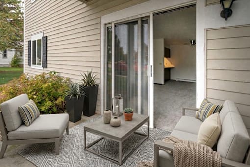 A patio with a grey couch, a grey chair, a grey coffee table and a grey rug.