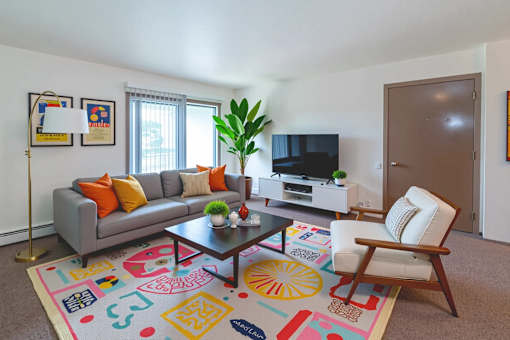 A living room with a grey couch, a coffee table, a chair, a plant, and a TV.