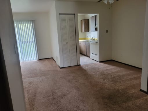 an empty living room with a door to a kitchen