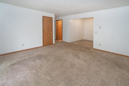 an empty living room with carpet and a door to a bedroom