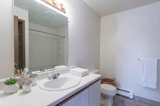 A white bathroom with a sink, mirror, toilet and a towel.