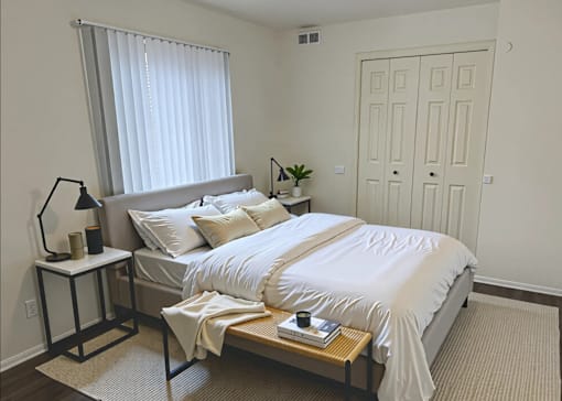A bedroom with a large bed and a window with blinds.