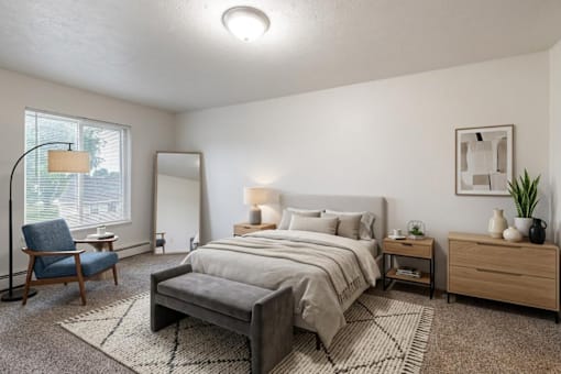 A well-lit bedroom with a large bed, a chair, and a nightstand.