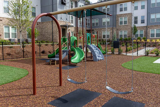 A playground with a green slide and a brown swing set.