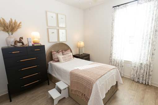A bedroom with a bed, nightstand, and a dresser with a vase on top.