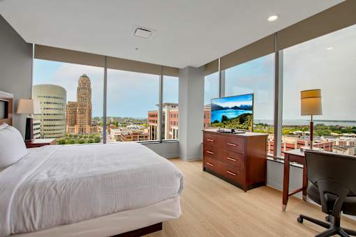 A bedroom with a large bed, a desk with a chair, and a view of the city.