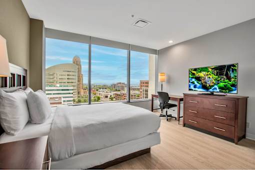 A bedroom with a large bed, a desk with a chair, and a flat-screen TV displaying a nature scene.