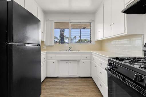 A black refrigerator sits in a kitchen with white cabinets and a black stove.