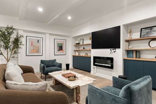 A living room with a brown couch, a blue chair, a white coffee table, a flat screen TV, and a fireplace.