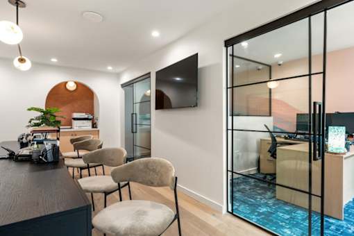 A modern office space with a wooden desk, chairs, and a television mounted on the wall.