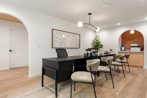 A black piano is in the middle of a room with a white wall and a framed picture above it.