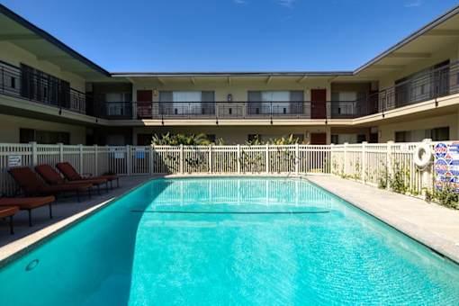 A swimming pool in front of a building with lounge chairs on the side.
