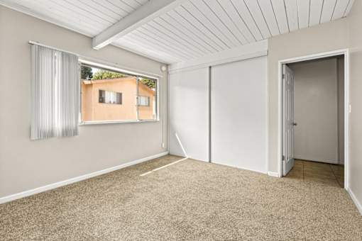 A room with a carpeted floor and a window showing a building outside.