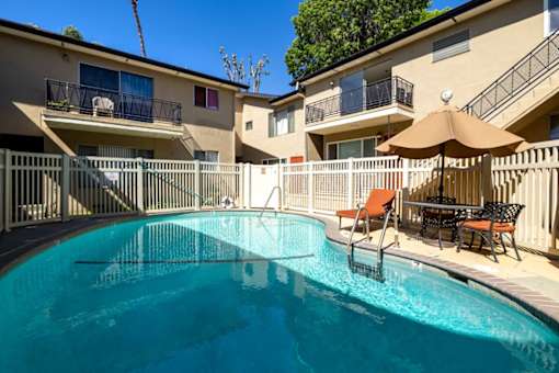 A swimming pool in a residential area with a sun umbrella and chairs.