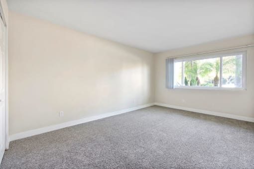 Apartments in Encino - White Oak Terrace - Interior View Of Bedroom Featuring Beige Carpets And Large Window Outlooking Palm Trees
