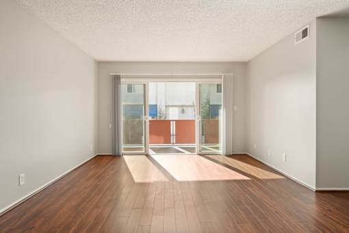 A room with a wooden floor and a glass door leading to a balcony.
