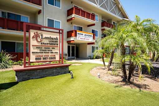 A sign for Lombardi Luxury Apartments is displayed in front of a building.