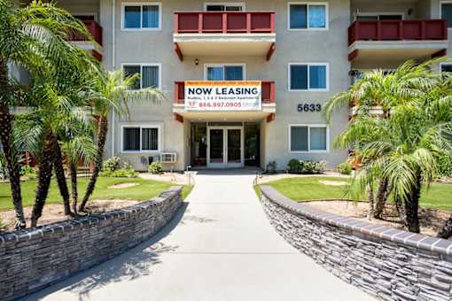 A building with a sign that says "NOW LEASING" is surrounded by palm trees.