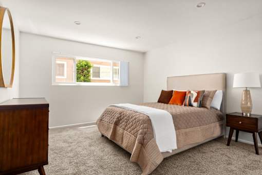 A bedroom with a bed, nightstand, lamp, and a mirror on the wall.