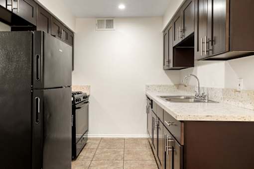 A kitchen with a black refrigerator and brown cabinets.