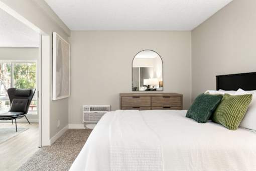 A bedroom with a large bed, a chair, and a mirror.
