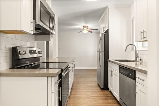 an empty kitchen with stainless steel appliances and white cabinets at Parkway Terrace Apartments, Culver City, California