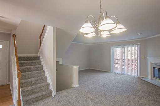 A living room with a grey carpet and a chandelier.
