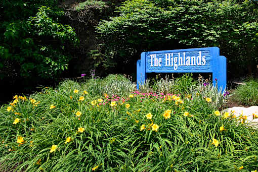 A blue sign that says "The Highlands" is surrounded by greenery and yellow flowers.