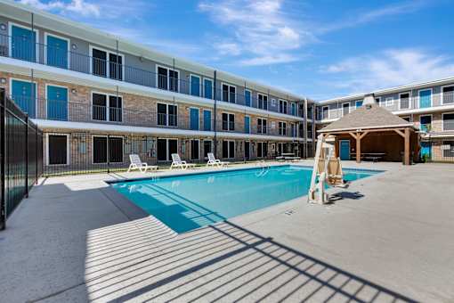 A swimming pool is surrounded by sun loungers in front of a building.
