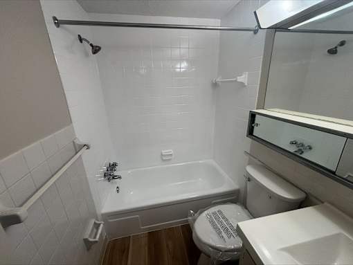 A white tiled bathroom with a toilet, sink, and bathtub.