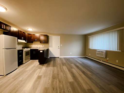 an empty kitchen and living room with plank flooring and white appliances