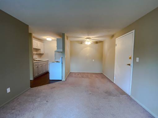 an empty living room with a kitchen and a ceiling fan in the dining area