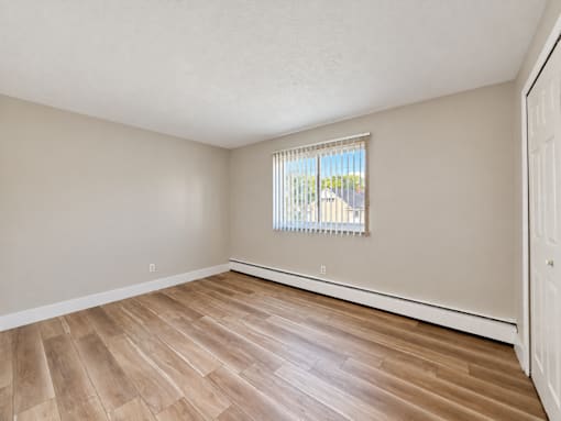 A room with wooden flooring and a window with blinds.