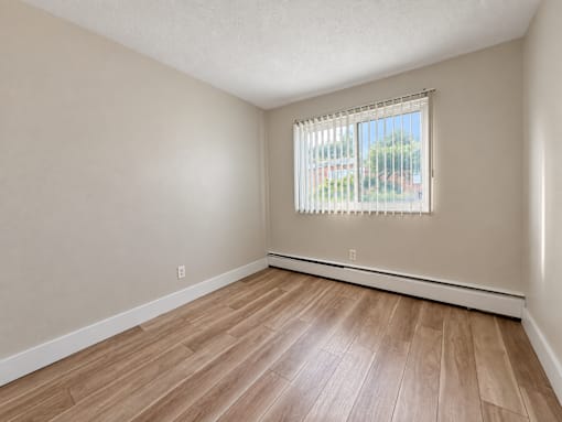 A room with wooden flooring and a window with blinds.