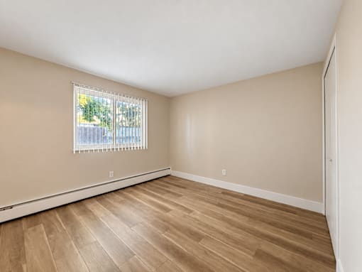 Empty room with wooden flooring and a window with blinds.