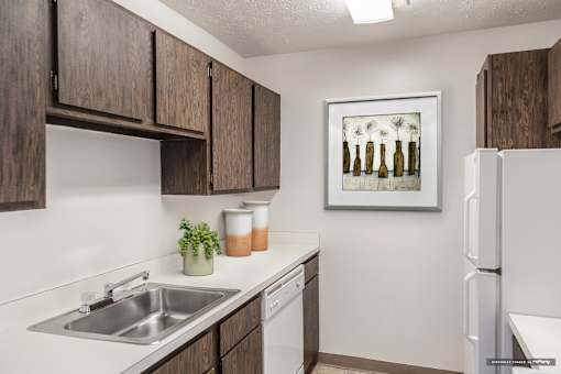 A kitchen with a white fridge, brown cabinets and a painting of bottles on the wall at Hummingbird Pointe & The Gardens, Parma, OH