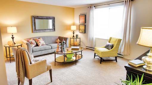 A living room with a grey couch, a yellow chair, and a coffee table at Hummingbird Pointe & The Gardens, Parma, Ohio