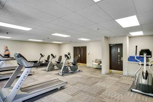 A gym with treadmills, elliptical machines, and a woman walking at Independence Place Apartments, Ohio 44130